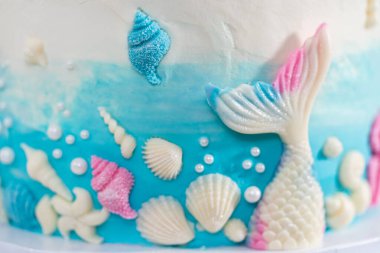 Deniz kızı temalı 3 katlı vanilyalı pasta çikolatalı deniz kızı kuyruğu ve deniz kabuğu ile süslenmiş beyaz pasta standı.