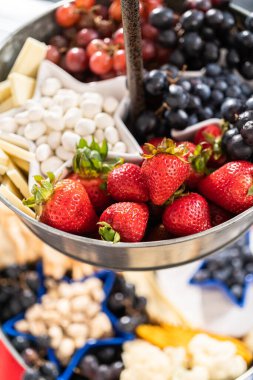 4 Temmuz şarküteri tahtası peynir, kraker, salam ve taze meyve dolu iki katlı bir metal tezgahta.