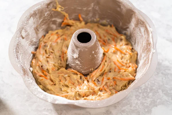Filling metal bundt cake pan with cake butter to bake carrot bundt cake with cream cheese frosting.