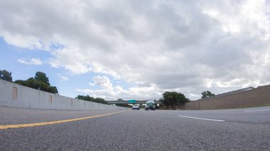 Bulutlu bir kış gününde, bir araba, Santa Maria, California yakınlarındaki 101. Otoyol boyunca bulutlu bir gökyüzünün altında, yeşil ve altın renkli bir karışımla sorunsuzca yol alır..