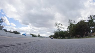 Bulutlu bir kış gününde, bir araba, Santa Maria, California yakınlarındaki 101. Otoyol boyunca bulutlu bir gökyüzünün altında, yeşil ve altın renkli bir karışımla sorunsuzca yol alır..