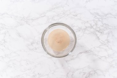 Flat lay. Activating dry yeast in a large glass mixing bowl to prepare the pizza dough.