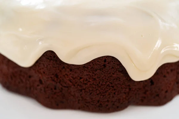 Pouring cream cheese glaze over freshly baked red velvet bundt cake.