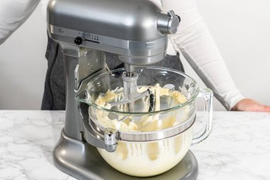 Whisking buttercream frosting in a glass mixing bowl with an electric kitchen mixer for American flag mini cupcakes.