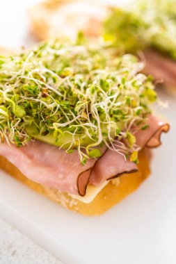 Assembling ham, cucumber, and sprout sandwiches on the white cutting board.