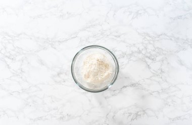 Flat lay. Mixing dry ingredients with a hand whisk in a large glass mixing bowl to bake mini vanilla cupcakes with ombre pink buttercream frosting.