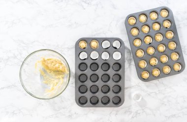 Flat lay. Scooping cupcake batter with dough scoop into a baking cupcake pan with liners to bake mini vanilla cupcakes with ombre pink buttercream frosting.