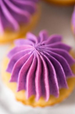 Beyaz pasta standında pembe tereyağlı taze pişmiş mini vanilyalı kekler..