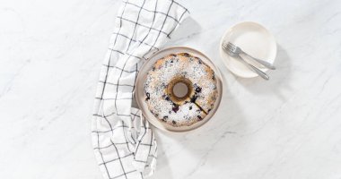 Düz yatıyordu. Taze pişmiş limonlu yaban mersinli kek dilimliyorum. Pudra şekerli..