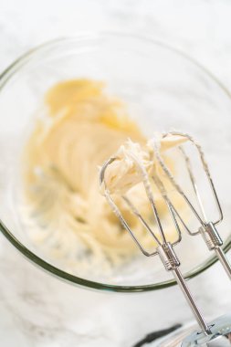 Mayasız tarçınlı çörekler için krem peynirli krema yapmak için karıştırma kabındaki malzemeleri karıştırıyorum..