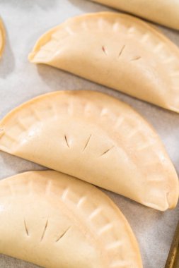 Fırınlanmamış kirazlı börekler, parşömen kağıdıyla kaplı fırın tepsisinde..