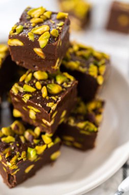 Homemade chocolate pistachio fudge square pieces on a white plate.