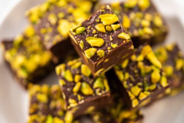 Homemade chocolate pistachio fudge square pieces on a white plate.