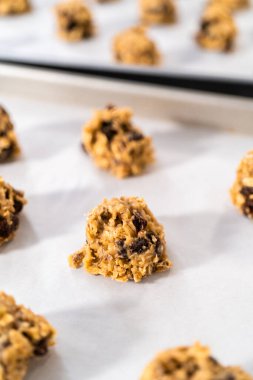 Yumuşak yulaf ezmeli, cevizli, kuru üzümlü kurabiye pişirmek için parşömen kağıdıyla kaplı bir yemek tepsisine hamur kepçesiyle kurabiye pişirmek..