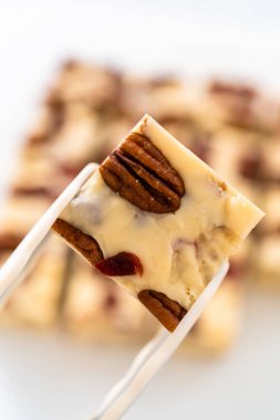 Beyaz çikolatalı fındıklı fındıklı şekerlemeyi beyaz bir kesme tahtasında küçük parçalara ayırmak..