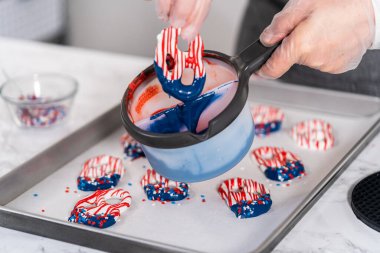 Dipping pretzels twists into melted chocolate to make red, white, and blue chocolate-covered pretzel twists.