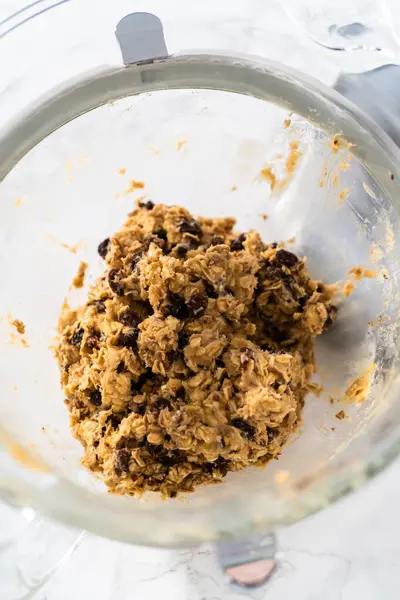 Scooping cookie dough with dough scoop into a baking sheet lined with parchment paper to bake soft oatmeal raisin walnut cookies.