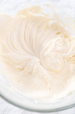 Krem peynirli krema hazırlamak için büyük bir bardakta karıştırma malzemeleri..