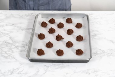 Scooping cookie dough with dough scoop into a baking sheet lined with parchment paper to bake chocolate cookies with chocolate hearts for Valentines Day.