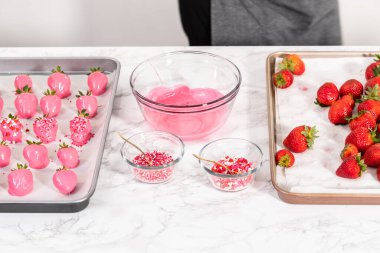 Çikolata kaplı çilekleri hazırlamak için erimiş çikolataya çilek bandırıyorum..