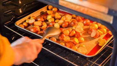 Modern bir mutfak ortamında, genç bir adam şu anda fırında baharatlı gökkuşağı patatesi kızartılarak lezzetli bir yemeğe doğru önemli bir adım atıyor..