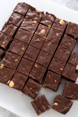 Büyük bir mutfak bıçağıyla çikolatalı macadamia şekerlemesini beyaz bir kesme tahtasında kare parçalara ayırmak..