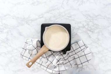 Flat lay. Heating whipped cream in a saucepan to make the white chocolate ganache frosting.