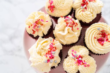 Taze pişmiş kadife kekler, üzerine beyaz çikolata ganache süslemesi serpilmiş..