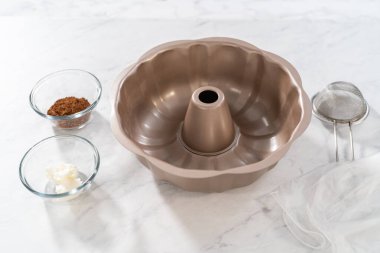 Greasing metal bundt cake pan with vegetable shortening and cocoa powder to bake gingerbread bundt cake with caramel filling.