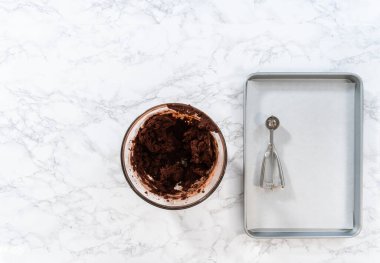 Flat lay. Scooping cookie dough with a small dough scoop into a baking sheet lined with parchment paper to bake peppermint white chocolate cookies.