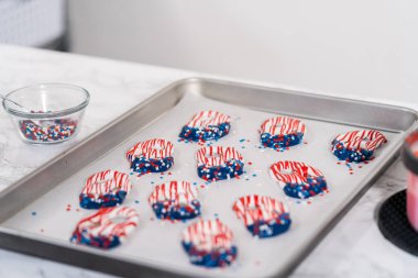 Dipping pretzels twists into melted chocolate to make red, white, and blue chocolate-covered pretzel twists.