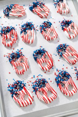 Dipping pretzels twists into melted chocolate to make red, white, and blue chocolate-covered pretzel twists.