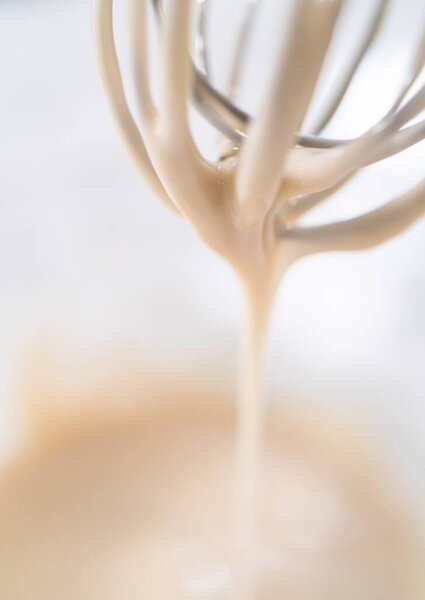 Lemon glaze. Mixing ingredients with a hand whisk in a glass mixing bowl to make lemon glaze.