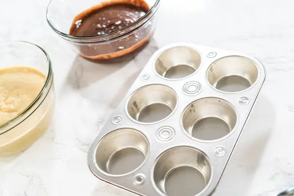 Cupcake foil liners are being meticulously filled with both chocolate and vanilla batter, setting the stage for the baking of deliciously diverse birthday cupcakes.