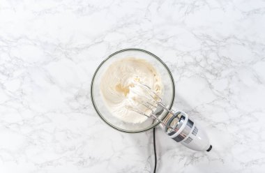 Flat lay. Whisking buttercream frosting in a glass mixing bowl with an electric hand mixer to prepare the peppermint buttercream frosting.