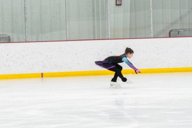 Artistik patinaj rutinini mükemmelleştiren genç bir kız kapalı bir buz pateni sahasında yarışma elbisesini giyerken.