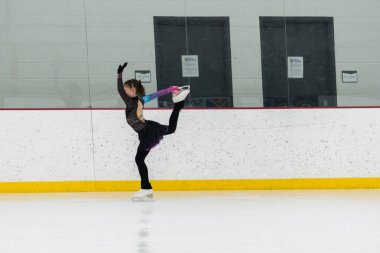 Artistik patinaj rutinini mükemmelleştiren genç bir kız kapalı bir buz pateni sahasında yarışma elbisesini giyerken.