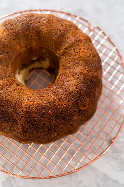 Removing freshly baked carrot bundt cake from the bundt cake pan to round the cooling rack.