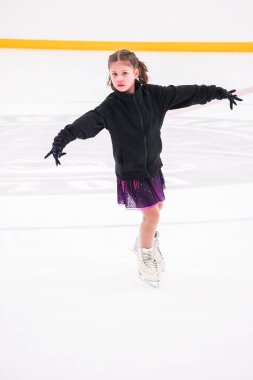 Küçük kız buz pateni pistinde artistik buz pateni yarışmasından önce pratik yapıyor..