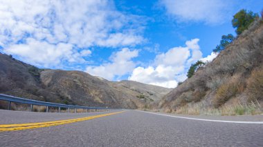 Araç, parlak güneşin altında Cuyama Otoyolu boyunca ilerliyor. Çevresindeki manzara, ışık saçan güneş ışığıyla aydınlanır ve araba seyahat ederken güzel ve davetkar bir sahne yaratır.