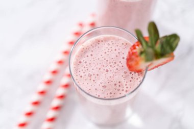 Taze taze çilek ve kağıt kamışla süslenmiş sağlıklı bir kahvaltı muzlu smoothie..