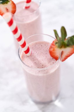 Taze taze çilek ve kağıt kamışla süslenmiş sağlıklı bir kahvaltı muzlu smoothie..