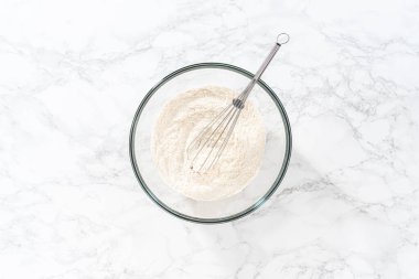 Flat lay. Mixing dry ingredients with a hand whisk in a large glass mixing bowl to bake American flag mini cupcakes.