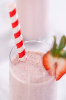 Taze taze çilek ve kağıt kamışla süslenmiş sağlıklı bir kahvaltı muzlu smoothie..