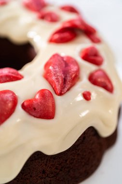 Freshly baked red velvet bundt cake with chocolate lips and hearts over cream cheese glaze for Valentines Day.