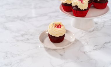 Taze pişmiş kadife kekler, üzerine beyaz çikolata ganache süslemesi serpilmiş..