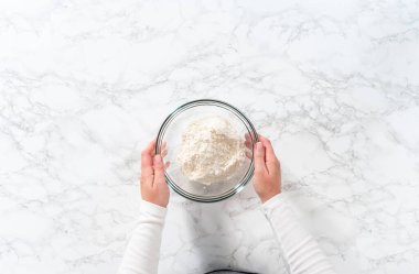 Flat lay. Mixing dry ingredients with a hand whisk in a large glass mixing bowl to bake mini vanilla cupcakes with ombre pink buttercream frosting.