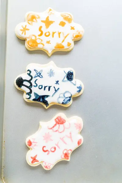 女の子の心温まるシーンを丁寧に書く食べ物の着色と砂糖クッキーに申し訳ありません クッキーは美しく白いロイヤルアイシングが殺到しました — ストック写真
