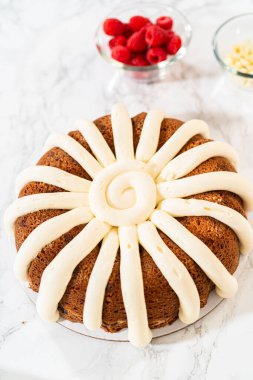 Hassasiyetle, Beyaz Çikolatalı Ahudududulu Çörek dikkatlice tavadan çıkartılır. Lezzetli krem peynirli kremayla süslenir ve lezzetli bir ziyafet yaratır..