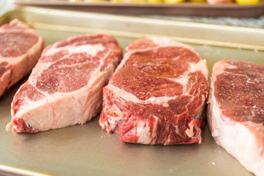 Modern beyaz bir mutfakta, baharatlı bir pirzola bifteği, güzel mermerleriyle övünerek, bir pişirme çarşafının üzerinde oturur. Açık hava gaz ızgarası için hazırlanıyor, mükemmel bir kavurucu söz veriyor.